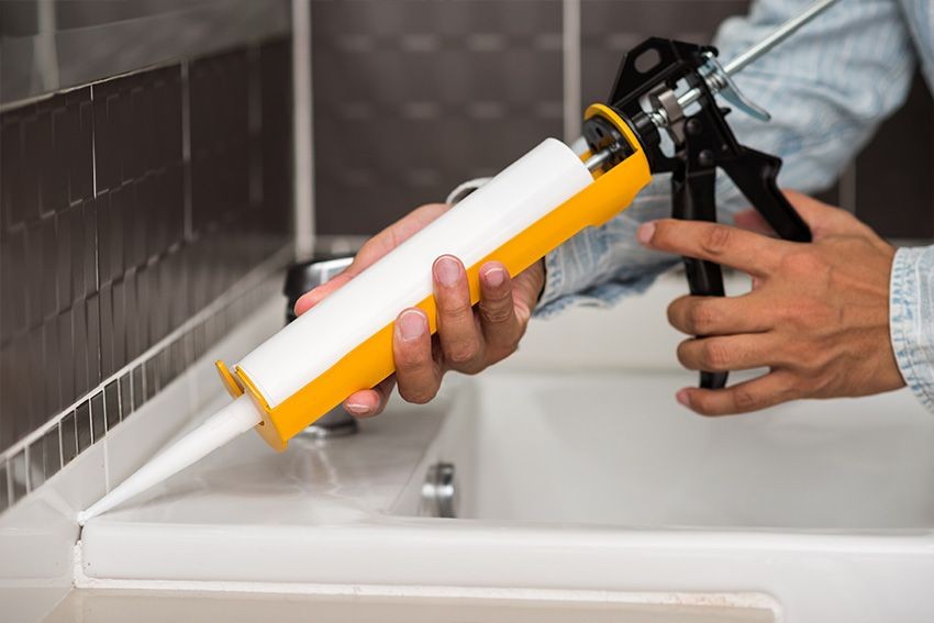 Person applying caulk to bathroom sink tiles using a caulking gun.