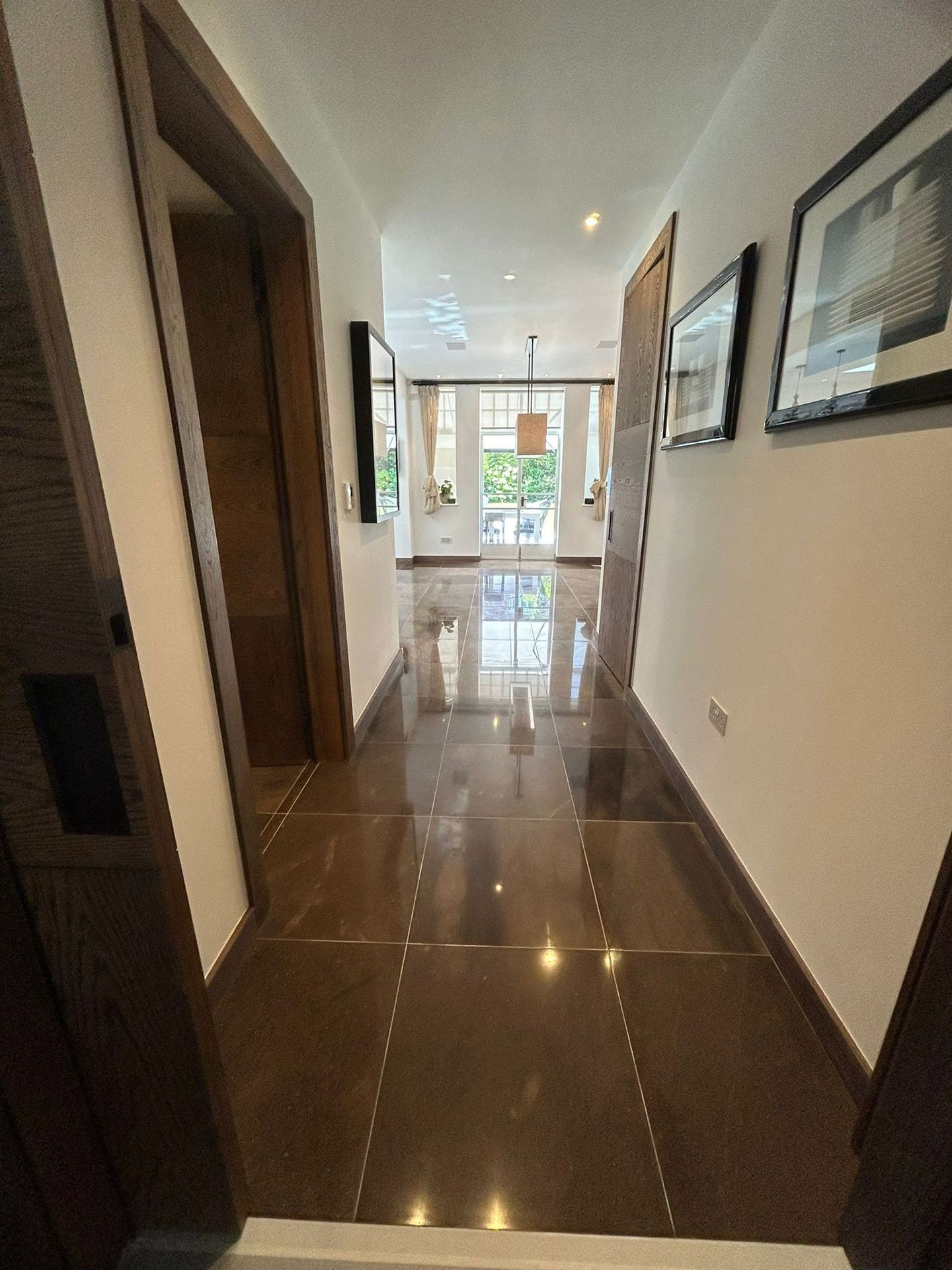 Modern hallway with glossy tiles, artwork on walls, and natural light from large windows.